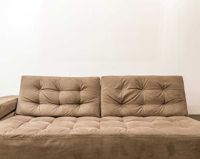 A white, tufted fabric sofa with rolled arms and dark wooden legs positioned against a paneled white wall in a well-lit room. The sofa surface appears clean and free of dust or stains, reflecting prof